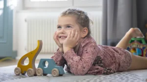 petite fille rêvant devant des jouets en bois à roulettes